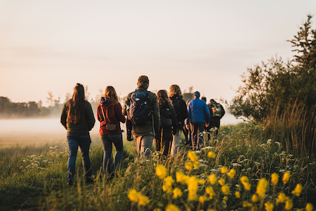 Een groep wandelaars kijkt in de verte naar de opkomende zon en de mist boven het gras